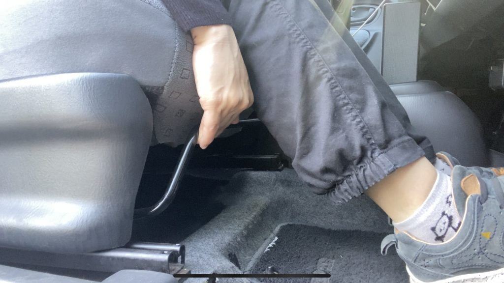 運転席のシートしたのレバーを調節して運転席の前後の位置を調整している